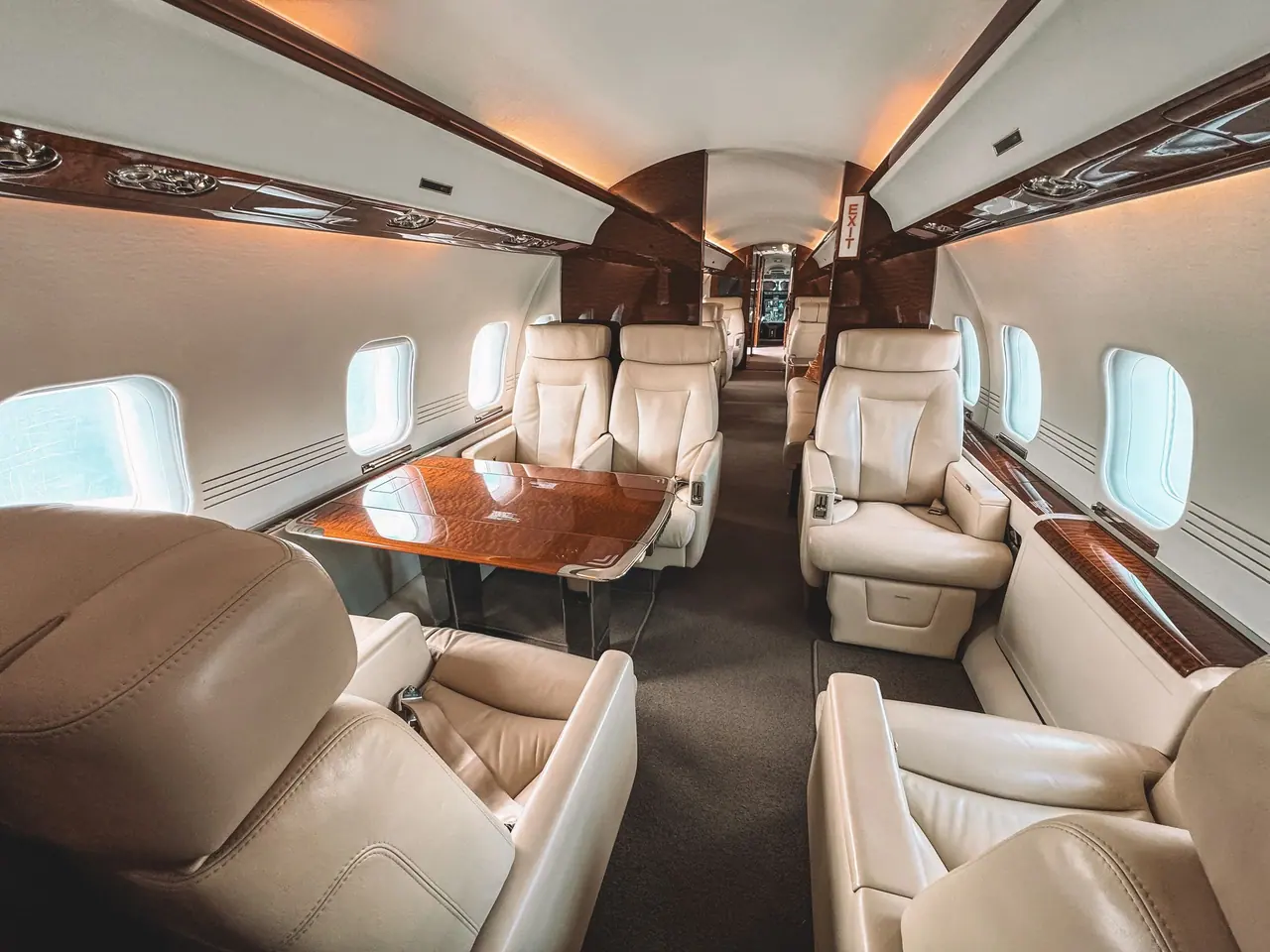 Business jet cabin with cream leather seats facing a polished wood table