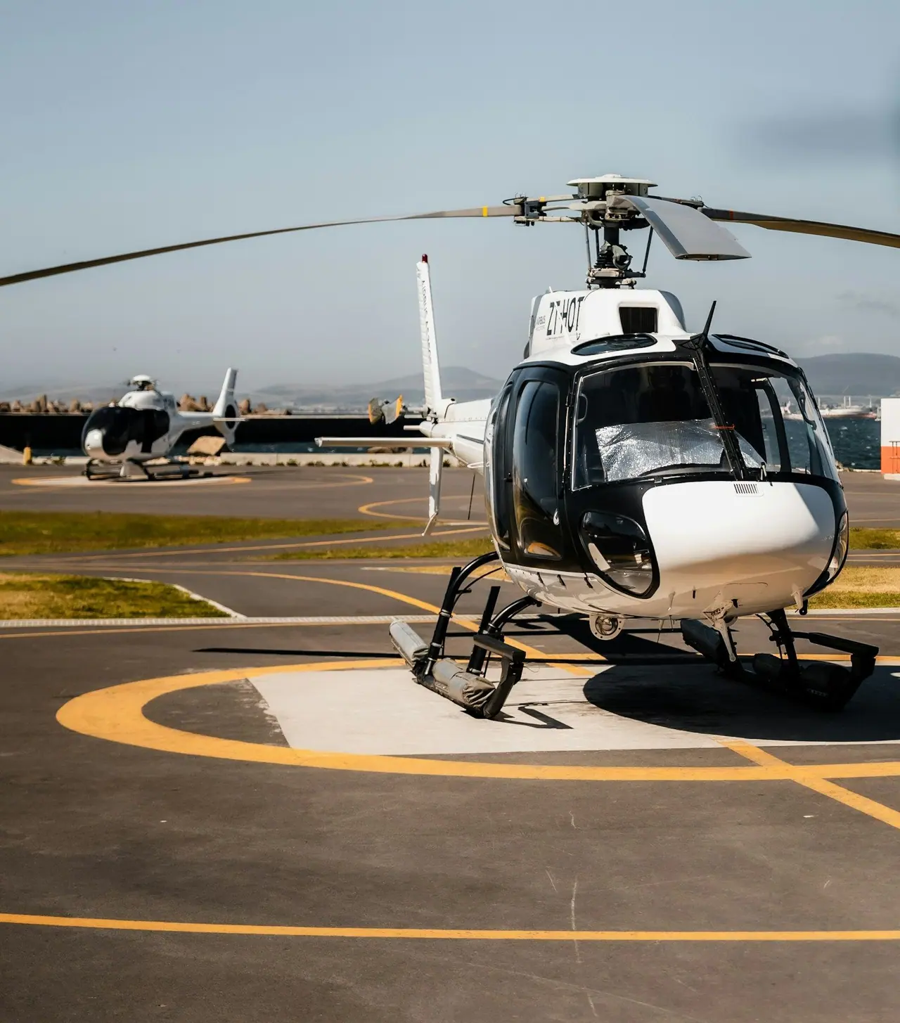 A white and black light helicopter parked on a helipad marked in yellow
