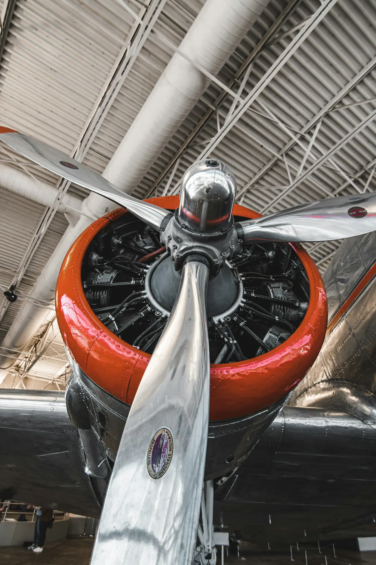 Polished propeller and spinner in front of a red radial engine, inside a hangar