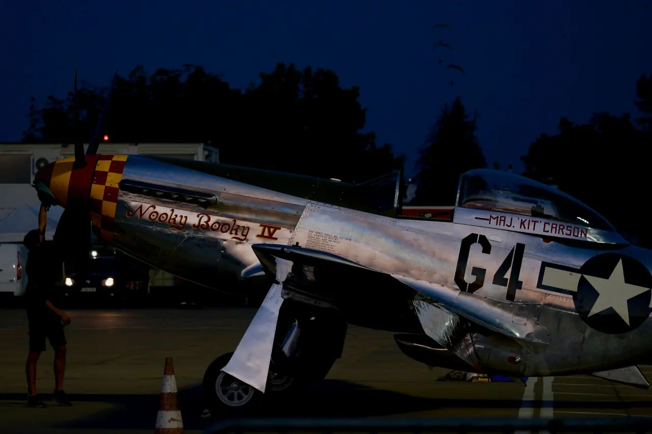 Polished bare-metal vintage fighter aircraft parked on the ramp at night